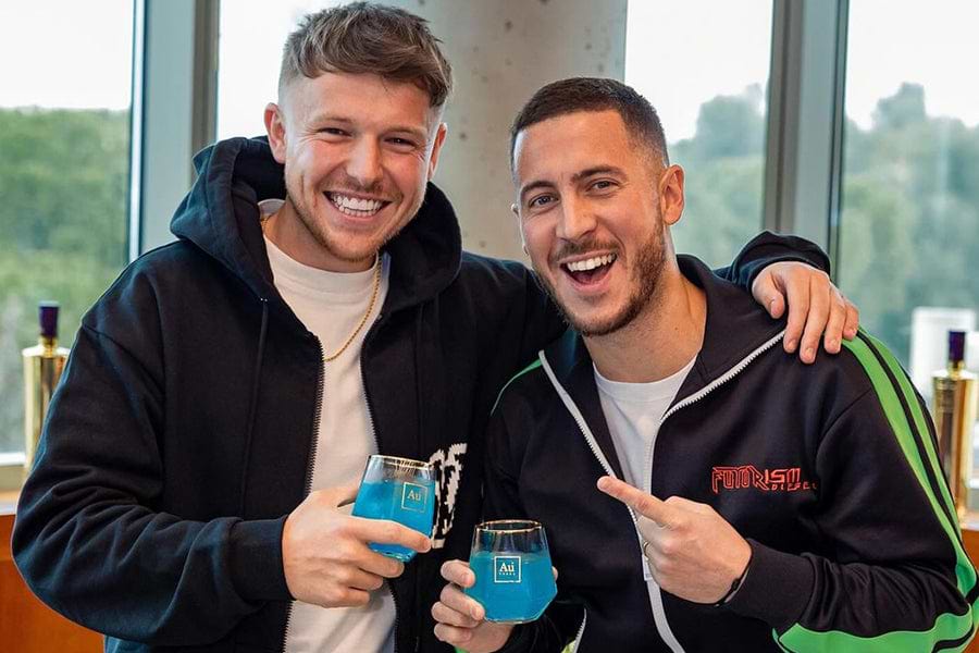 Two men smiling, holding blue drinks in glasses with the Au logo