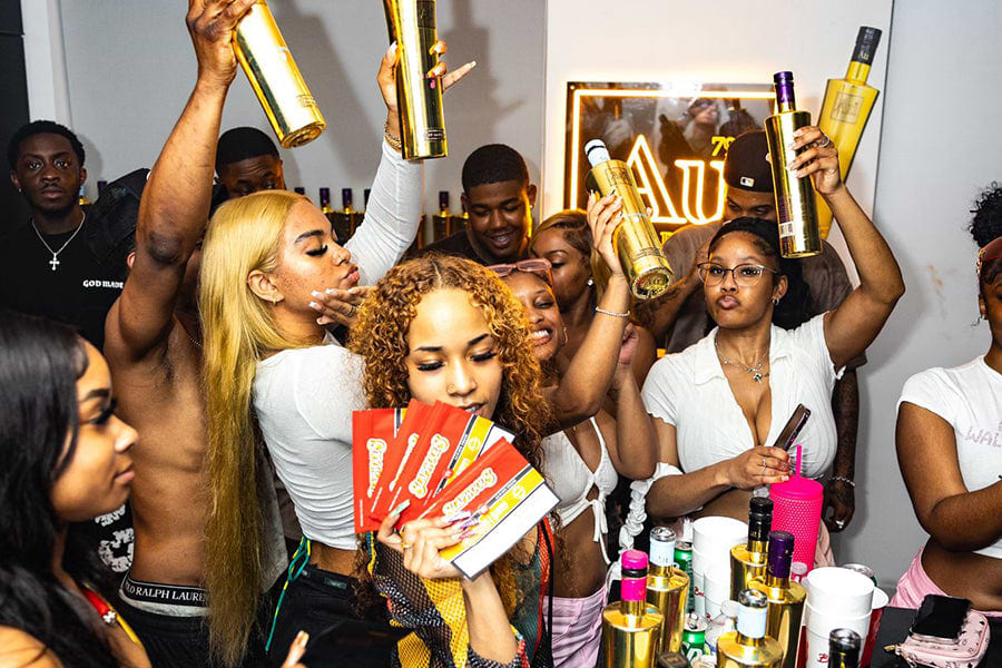 Group of people holding up gold bottles and red packages at a party
