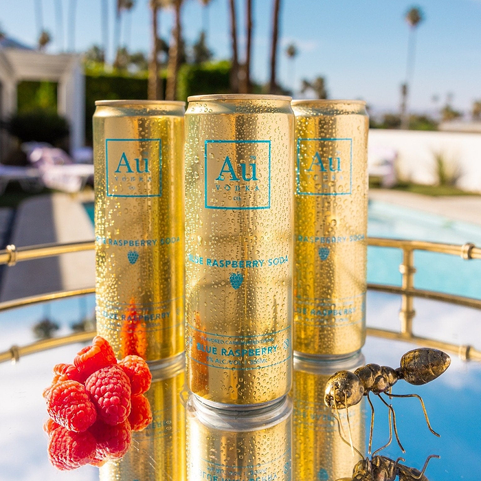 Three Au Vodka Blue Raspberry Soda cans on a tray with raspberries and an ant