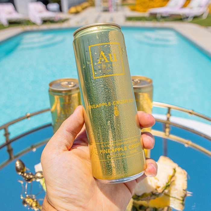 Hand holding an Au Vodka USA Pineapple Crush can with water droplets, by a pool