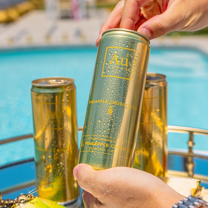 Hand picking up an Au Vodka USA Pineapple Crush can from a tray by a pool