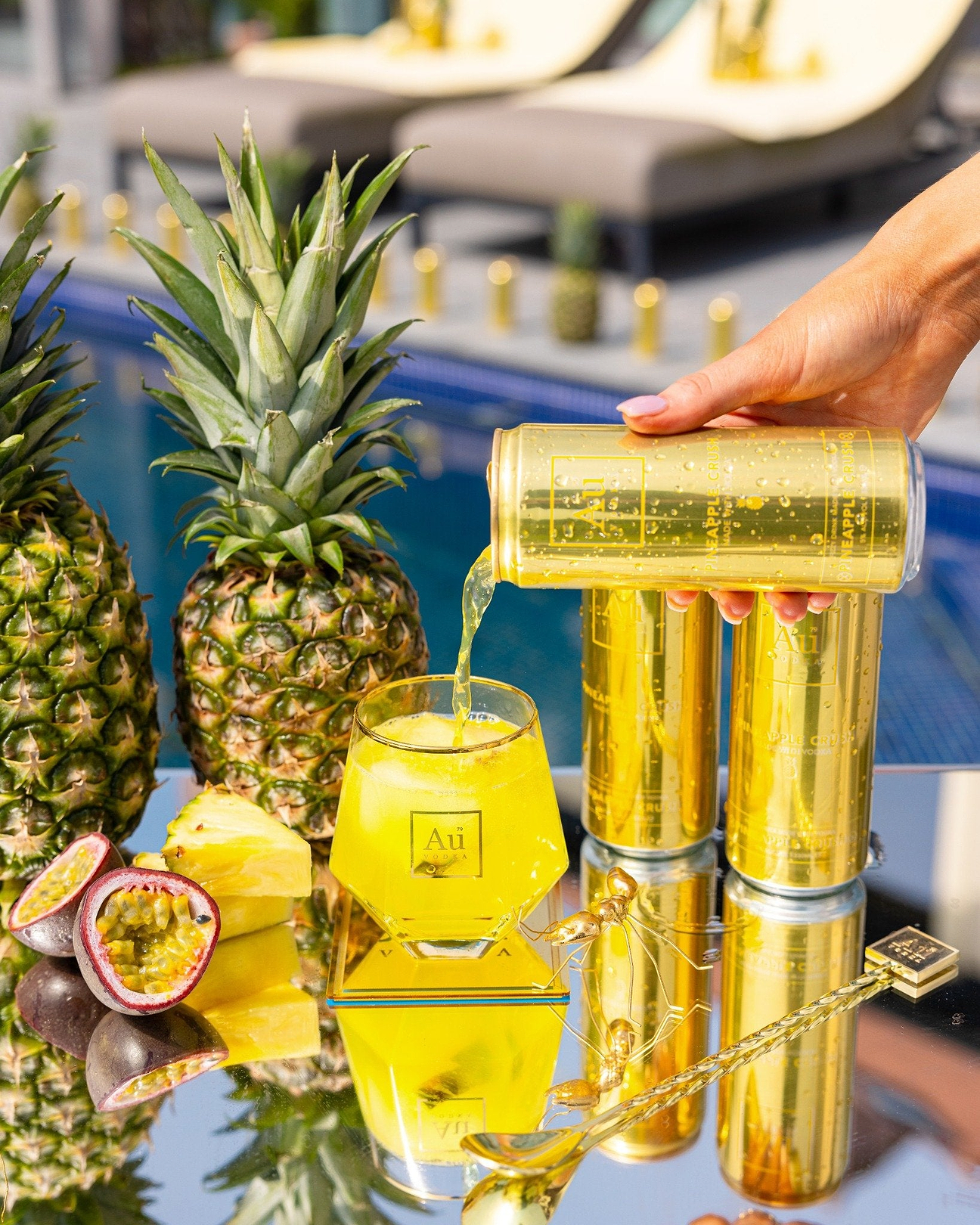 Au Vodka Pineapple Crush being poured into a glass with fresh pineapple and passion fruit by a pool