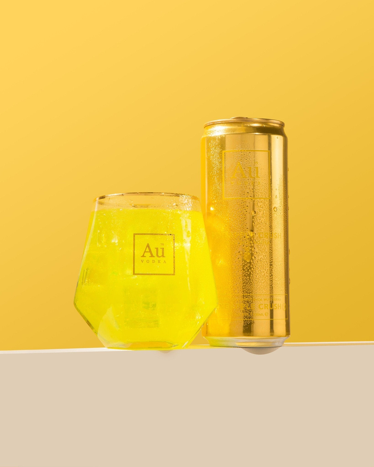 Au Vodka Pineapple Crush can and glass of yellow drink on a yellow background