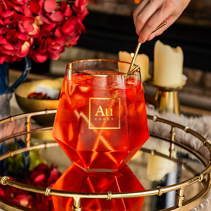 Au Vodka branded faceted glassware containing a red cocktail with strawberries and a gold stirring spoon