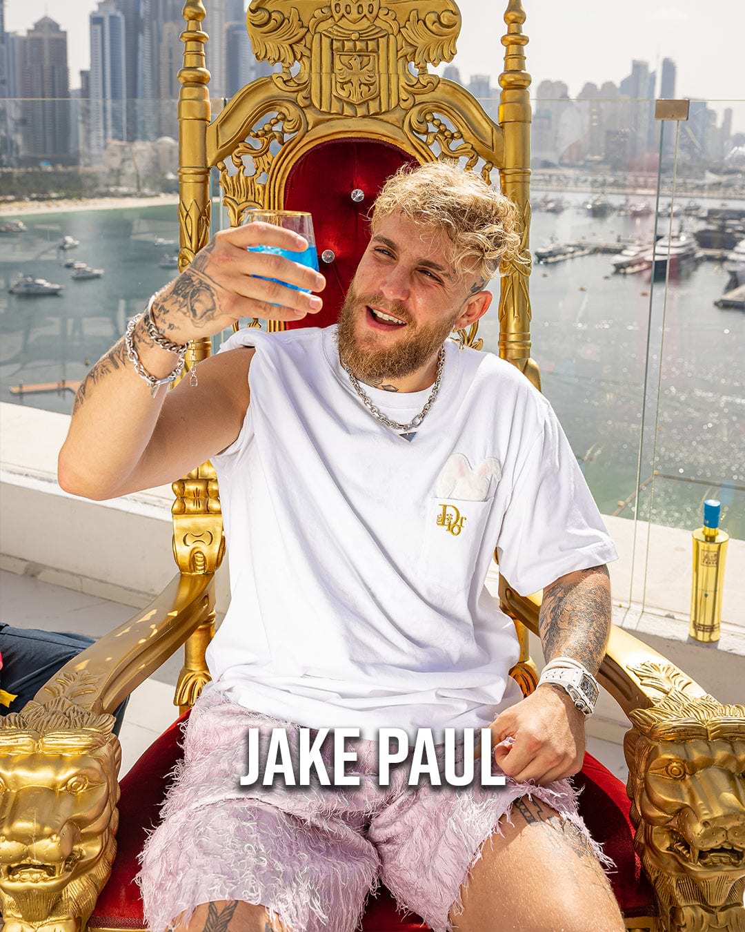 Jake Paul sitting on a golden throne, holding a blue drink, with a city and harbor in the background