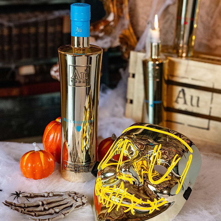 Au Vodka Blue Raspberry bottle with Halloween decor including a gold mask and mini pumpkins