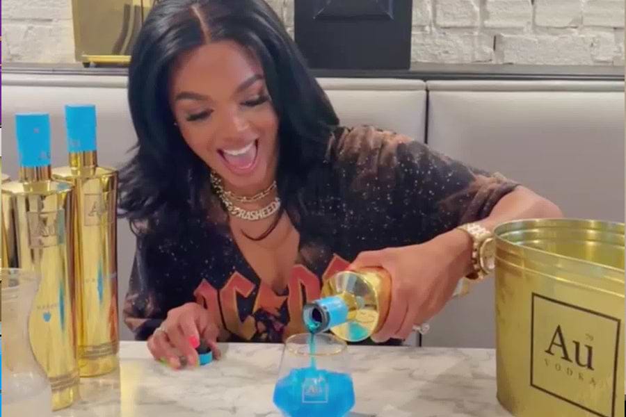 Woman pouring blue Au Vodka into a glass, with gold Au Vodka bottles and bucket on the table