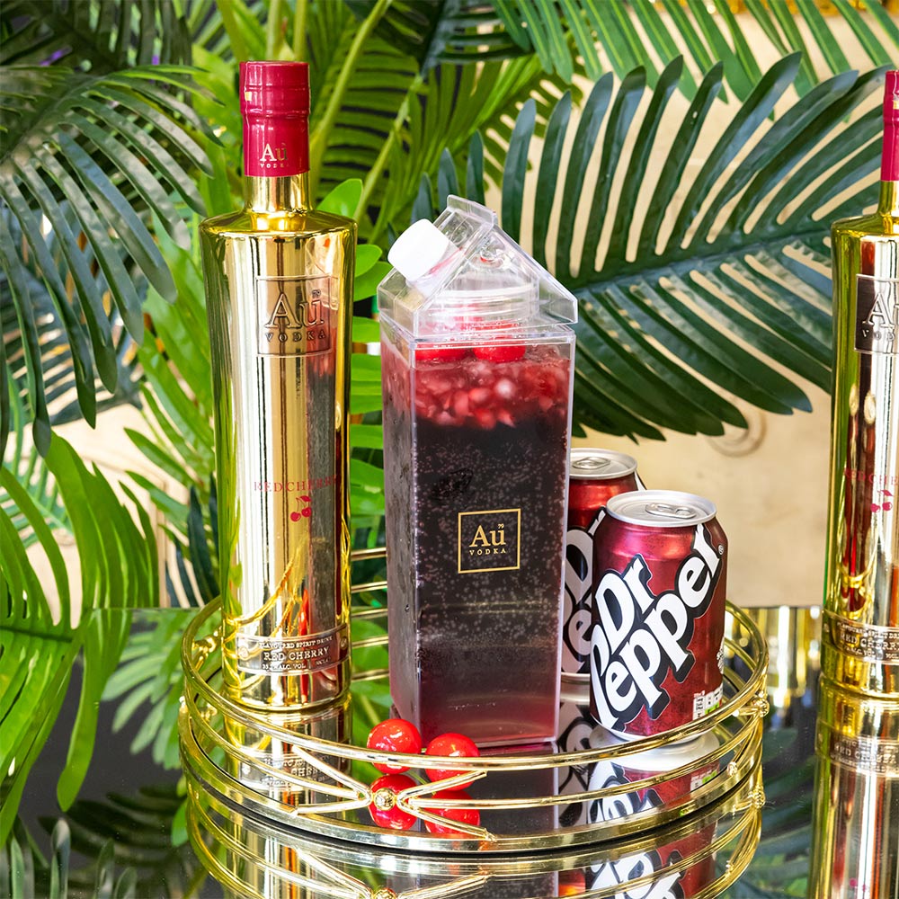 Au Vodka bottle next to a clear carton of dark cocktail and a can of Dr Pepper