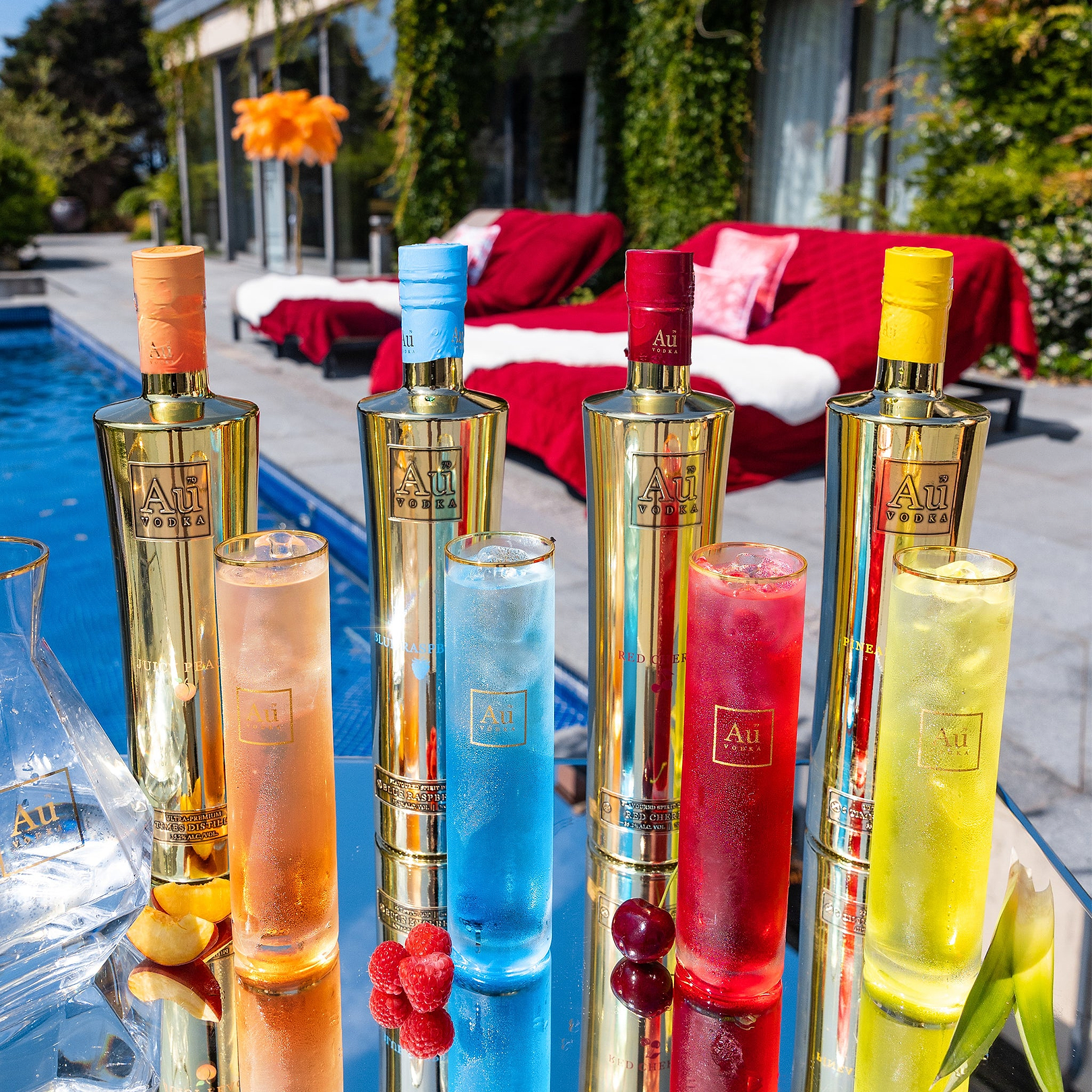 Four Au Vodka gold bottles and matching colorful cocktails by a swimming pool