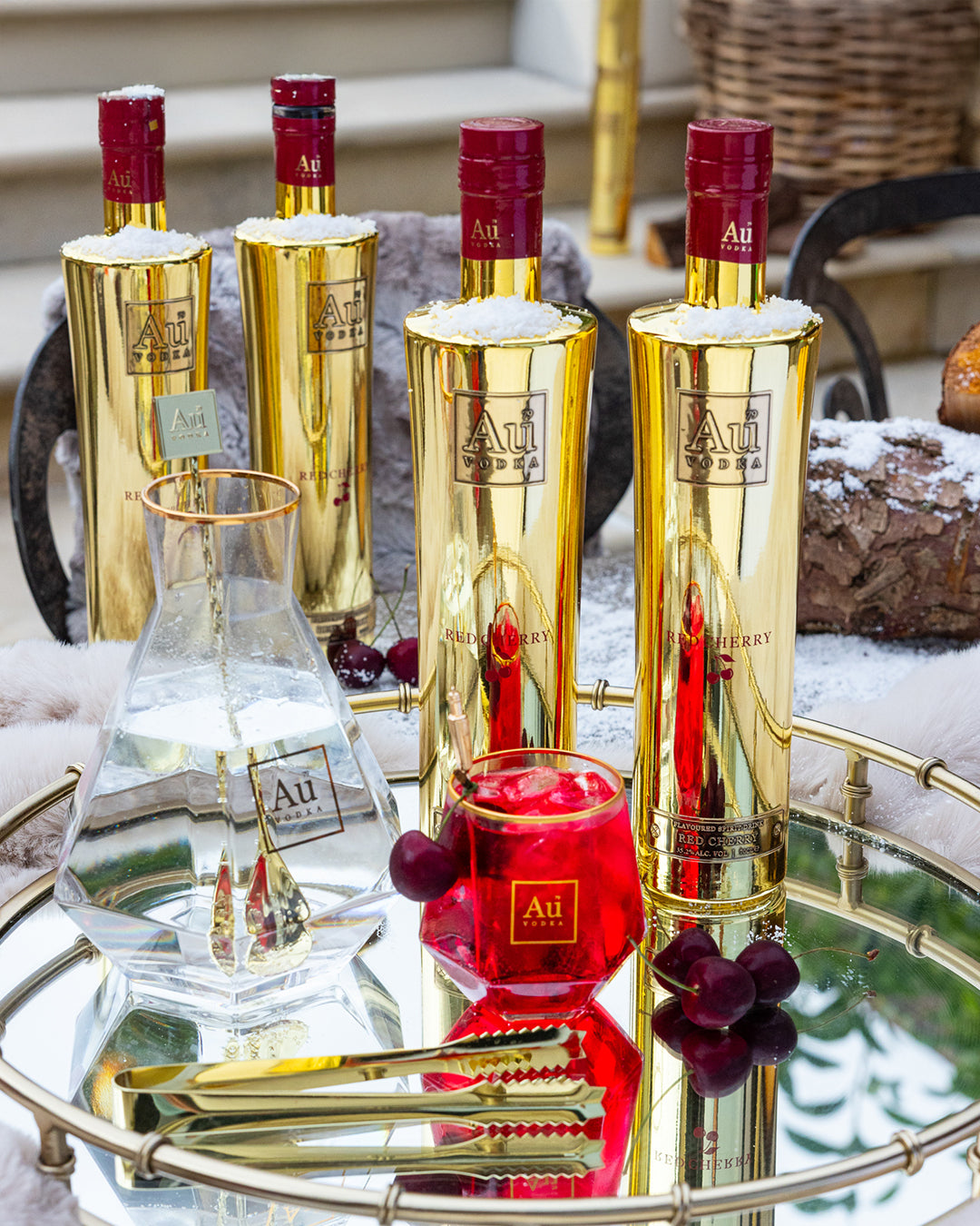 Au Vodka Red Cherry bottles and a glass of red cocktail on a mirrored tray with fresh cherries