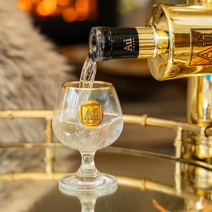 Au Vodka being poured from a gold bottle into a branded Au Vodka glassware snifter