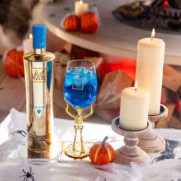 Au Vodka Blue Raspberry bottle and skeleton stem glass with blue cocktail surrounded by candles and pumpkins