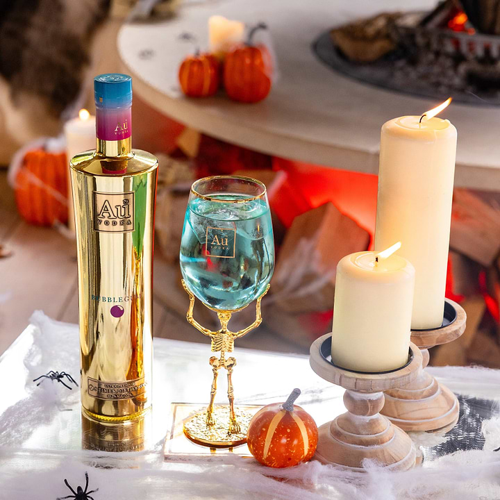 Au Vodka Bubblegum bottle and skeleton stem glass with blue cocktail surrounded by candles and pumpkins