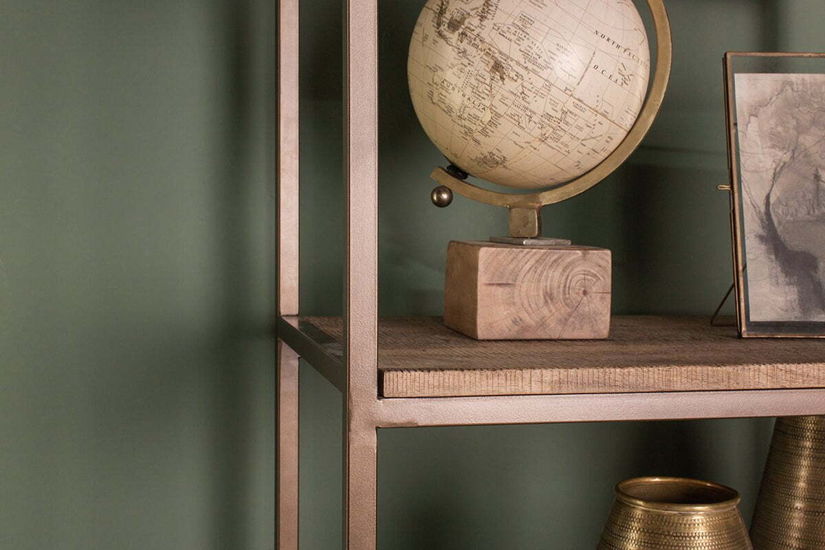 A close-up of the nkuku Marjori Mango Wood And Iron Standing Shelves - Wide against a green wall, styled with a vintage globe on a wooden base, a framed picture, and two metallic vases (one partly visible in the bottom right).