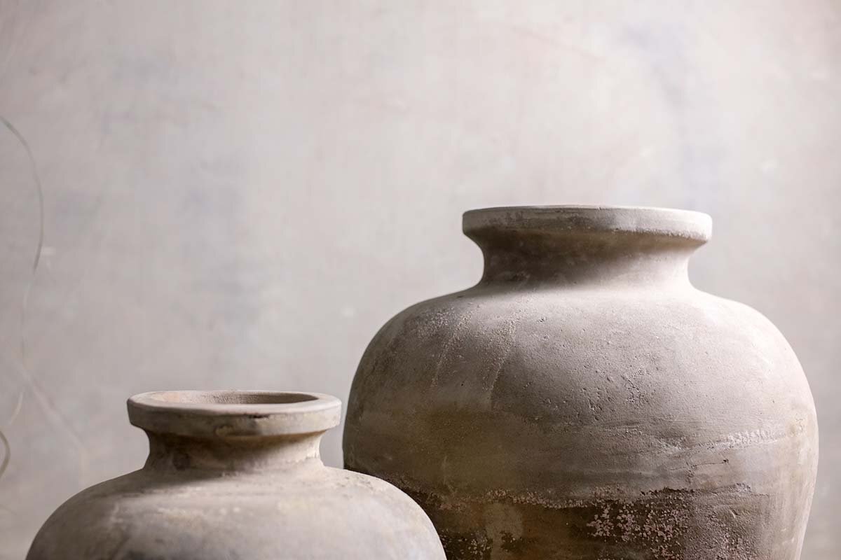 Two Affiti Clay Tapered Pots - Large by nkuku, with wide openings and matte, earthy textures, sit side by side against a light gray background, highlighting their rustic, handmade appeal.