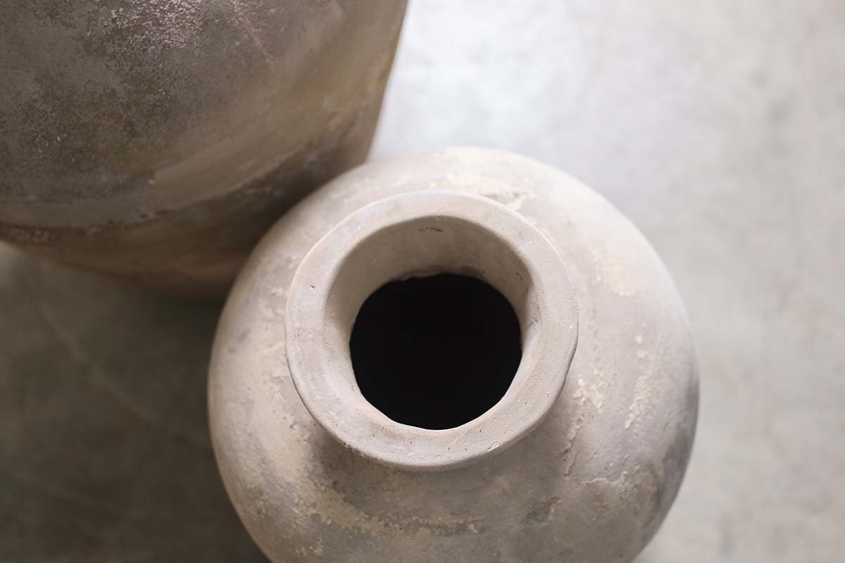 Close-up, top-down view of the nkuku Affiti Clay Tapered Pot - Large on a smooth, light surface. The wide-mouthed urn is prominent in front, with the edge of a second pot partially visible in the upper left corner.