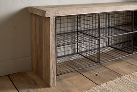 The nkuku Abha Reclaimed Wood & Iron Storage Bench - Natural features six open wire mesh cubbies, making it a perfect entryway organizer for your hallway. It sits stylishly on a wooden floor by a beige wall and woven rug.