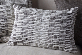 The nkuku Aahna Wool Cushion Cover in Charcoal features a textured, woven design in gray and white wool and recycled polyester, styled here on a light fabric sofa with coordinating cushions in the background.