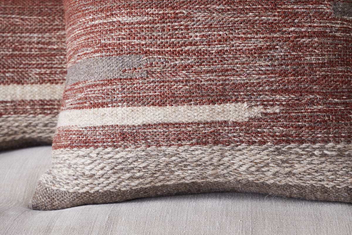 A close-up of the nkuku Aakash Wool Cushion Cover in rust showcases its vibrant color and luxurious wool texture.