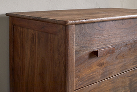 Close-up of the nkuku Anbu Acacia Chest of Drawers in Washed Walnut, showcasing its smooth natural wood grain, rectangular handle, and rounded top edges—an ideal bedroom storage piece against a light wall.