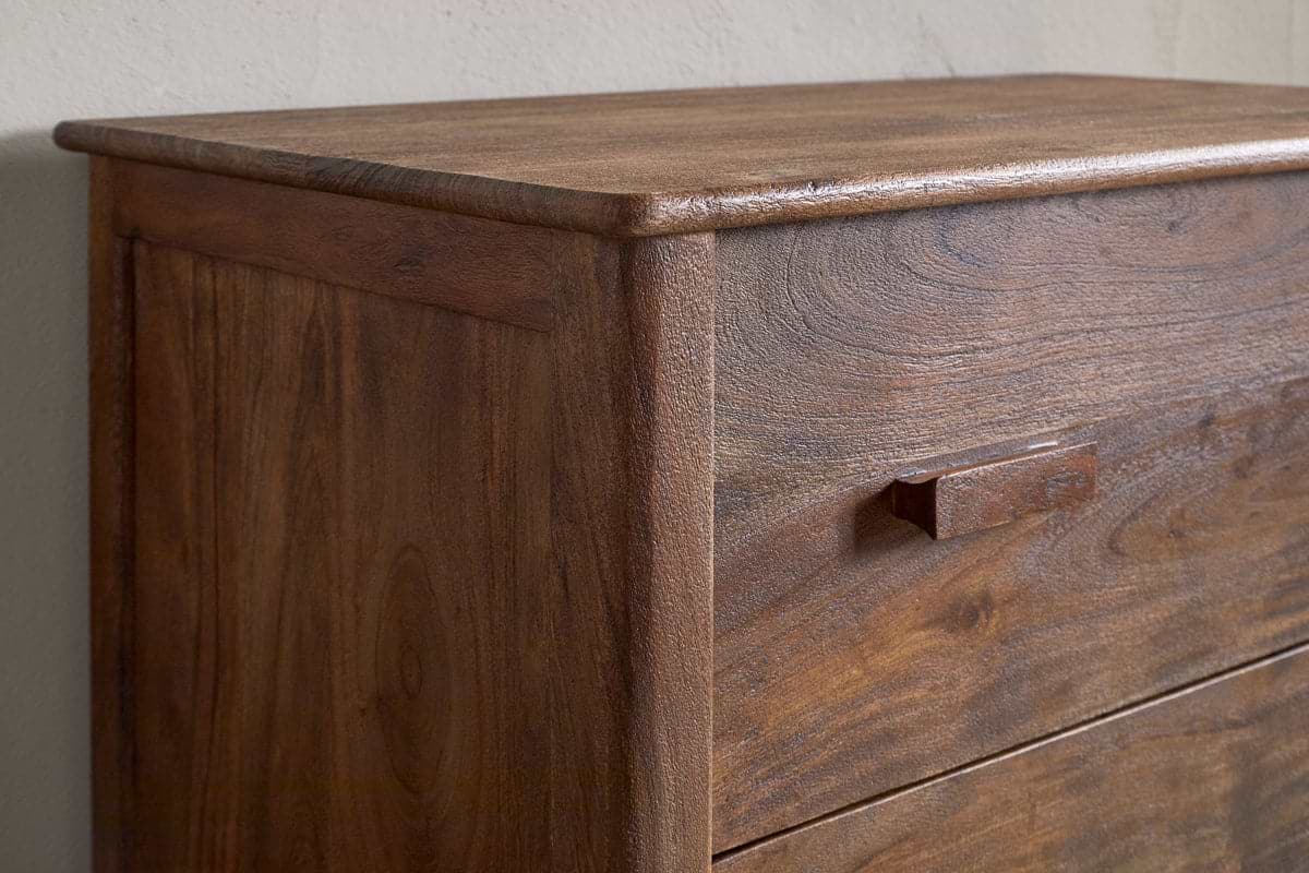 Close-up of the nkuku Anbu Acacia Chest of Drawers in Washed Walnut, showcasing its smooth natural wood grain, rectangular handle, and rounded top edges—an ideal bedroom storage piece against a light wall.