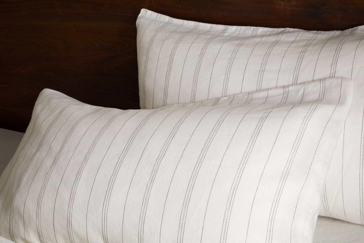 Two pillows in nkukus Anta Hemp & Cotton Housewife Pillowcases in sage green are neatly arranged against a dark wooden headboard, with one pillow slightly overlapping the other.