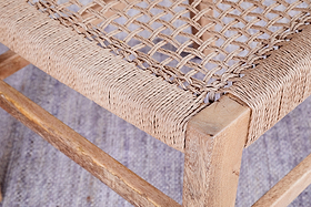 Close-up of the Aamani Mango Wood & Cord Dining Chair by nkuku, showing its natural mango wood frame with visible grain and a tightly woven cord seat in a textured crisscross pattern. The chair sits on a light, textured floor.