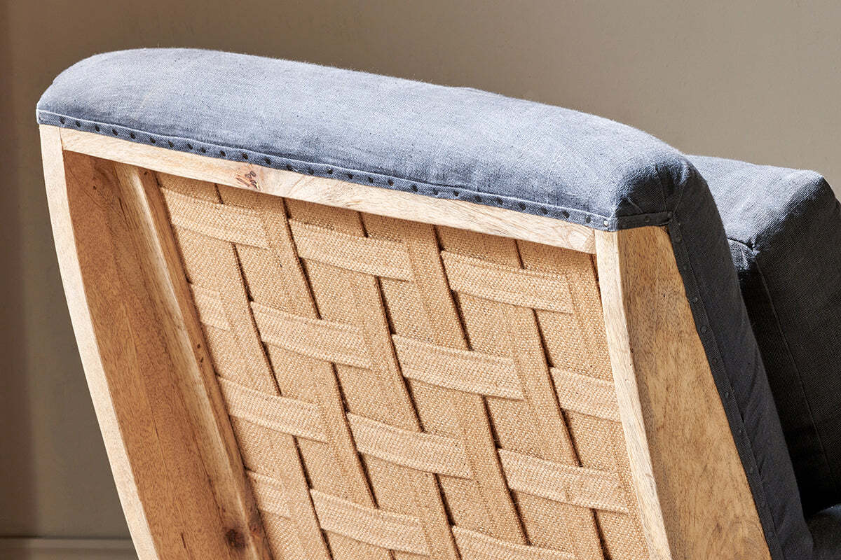 Close-up of the Abe Deconstructed Linen Armchair by nkuku, featuring a cushioned backrest in textured charcoal linen upholstery and a light natural mango wood frame, highlighted softly by sunlight.