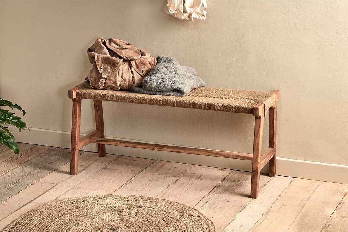 The nkuku Amhara Acacia & Jute Woven Bench is topped with a brown leather bag and gray sweater. In front, a round jute rug on the wooden floor highlights the space's natural textures.
