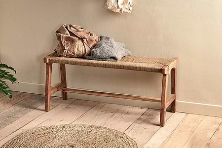 The nkuku Amhara Acacia & Jute Woven Bench is topped with a brown leather bag and gray sweater. In front, a round jute rug on the wooden floor highlights the space's natural textures.