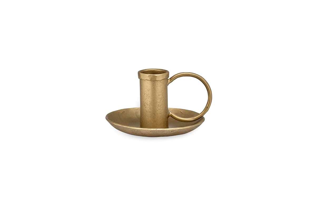 The Amri Iron Candlestick by nkuku features an antique brass finish, a round base, a short holder for dinner candles, and a large circular side handle—all displayed on a plain white background.