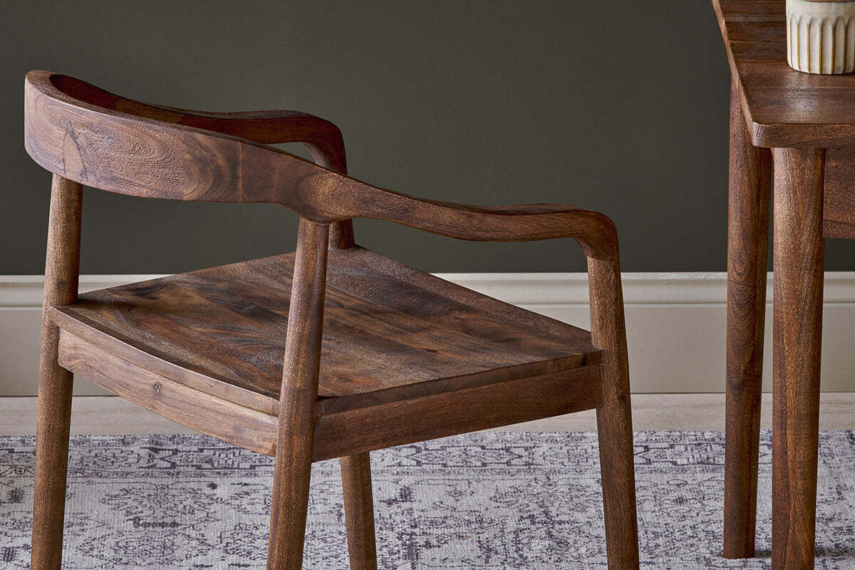 A close-up of the Anbu Acacia Dining Chair by nkuku features a curved back and arms, showcasing the washed walnut finish, visible acacia wood grain, and refined craftsmanship.