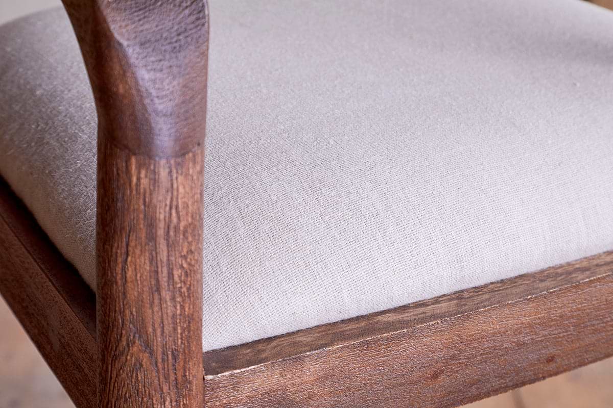 Close-up of the nkuku Anbu Acacia Upholstered Counter Chair - Washed Walnut, featuring a frame and armrest in natural-grain acacia wood and tightly stretched light beige upholstery for a soft, refined look.