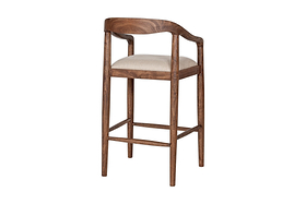 The nkuku Anbu Acacia Upholstered Counter Chair in Washed Walnut features a curved backrest, rounded armrests, four slender legs with footrests, and a light beige seat. Smooth polished finish. Plain white background.
