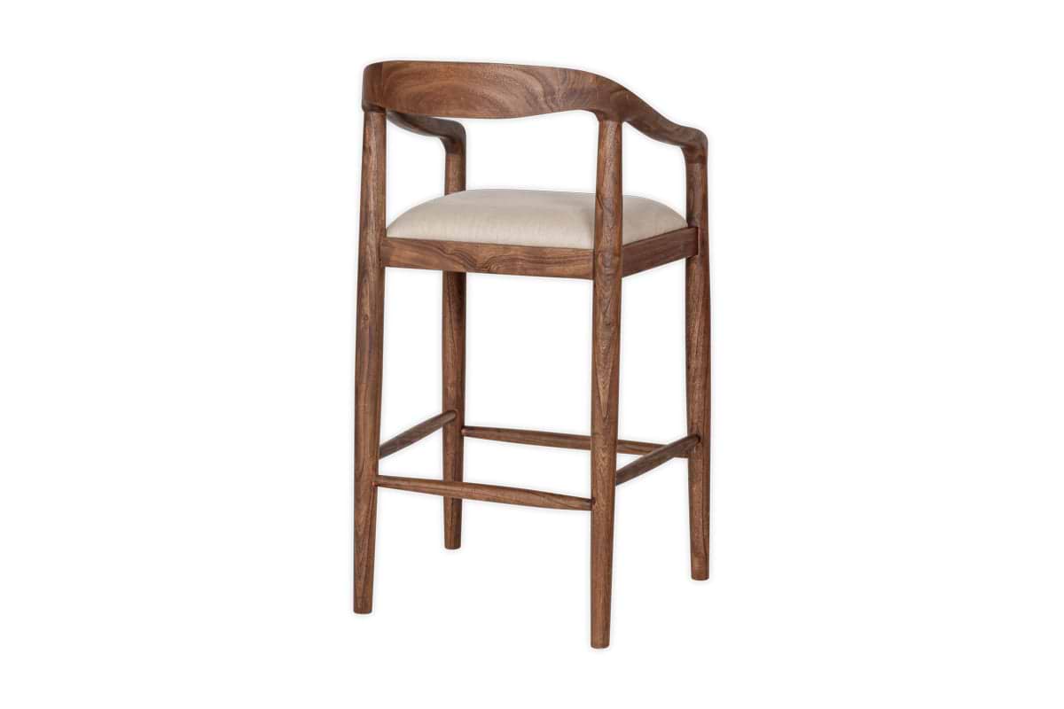The nkuku Anbu Acacia Upholstered Counter Chair in Washed Walnut features a curved backrest, rounded armrests, four slender legs with footrests, and a light beige seat. Smooth polished finish. Plain white background.