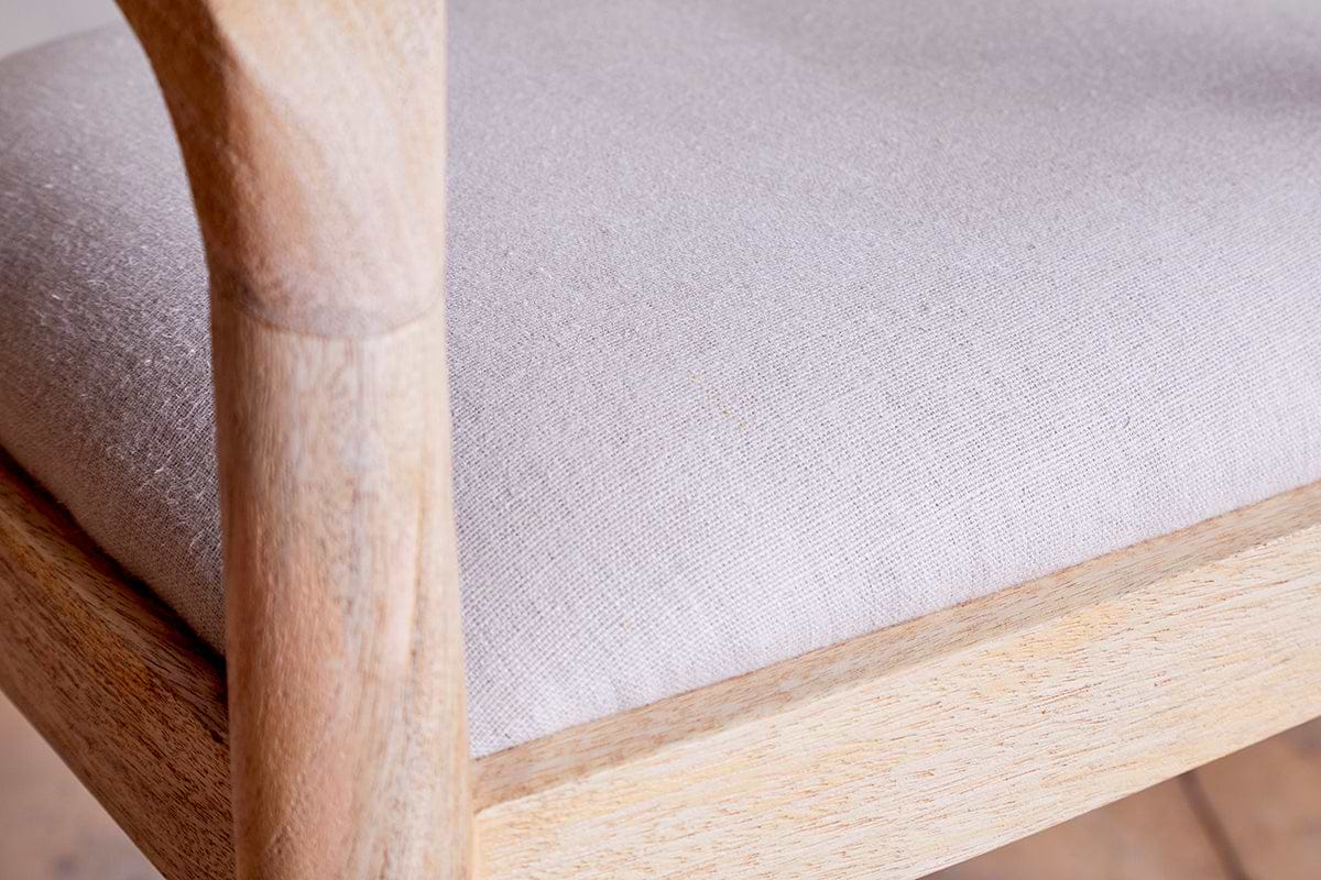 Close-up of the nkuku Anbu Mango Wood Upholstered Counter Chair - Natural, featuring a textured light beige cushion, smooth rounded armrests, and a minimalist frame highlighting the natural wood grain and light finish.