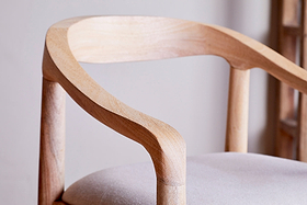 Close-up of the nkuku Anbu Mango Wood Upholstered Counter Chair - Natural, featuring a curved armrest and backrest in smooth, light mango wood with natural grain, and a seat upholstered in light neutral fabric for a minimalist look.