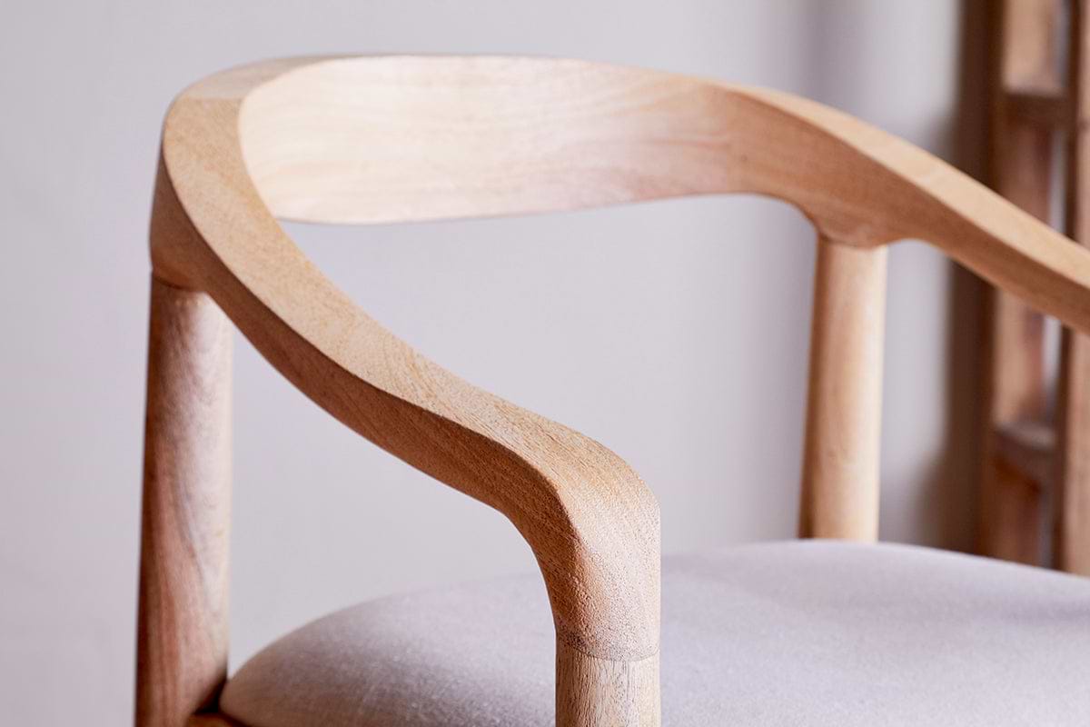 Close-up of the nkuku Anbu Mango Wood Upholstered Counter Chair - Natural, featuring a curved armrest and backrest in smooth, light mango wood with natural grain, and a seat upholstered in light neutral fabric for a minimalist look.