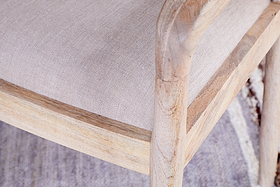 Close-up of the nkuku Anbu Mango Wood Upholstered Dining Chair - Natural, showcasing its neutral linen seat, light mango wood frame, textured fabric, and visible natural wood grain.