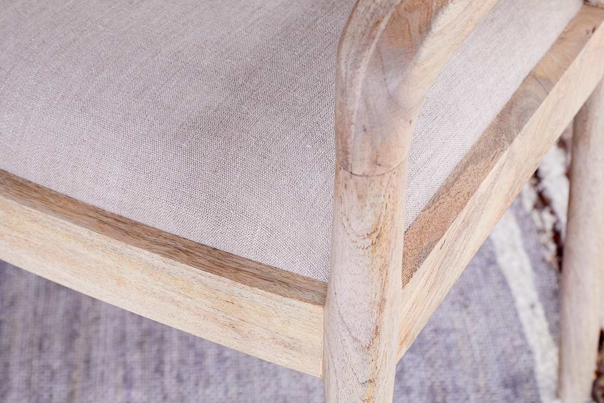 Close-up of the nkuku Anbu Mango Wood Upholstered Dining Chair - Natural, showcasing its neutral linen seat, light mango wood frame, textured fabric, and visible natural wood grain.