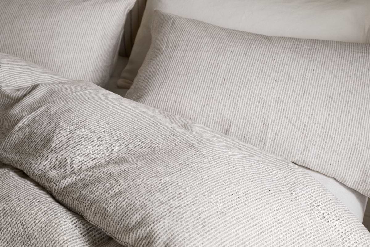 Close-up of a neatly made bed with beige and white pinstriped bedding, featuring the nkuku Borba Hemp & Cotton Duvet Cover in Espresso, along with pillows, creating a cozy and inviting look.