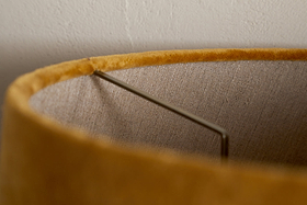 Close-up of the Batakha Velvet & Linen Lampshade in Dark Ochre by nkuku, highlighting its metal frame and textured inner lining against a white wall.