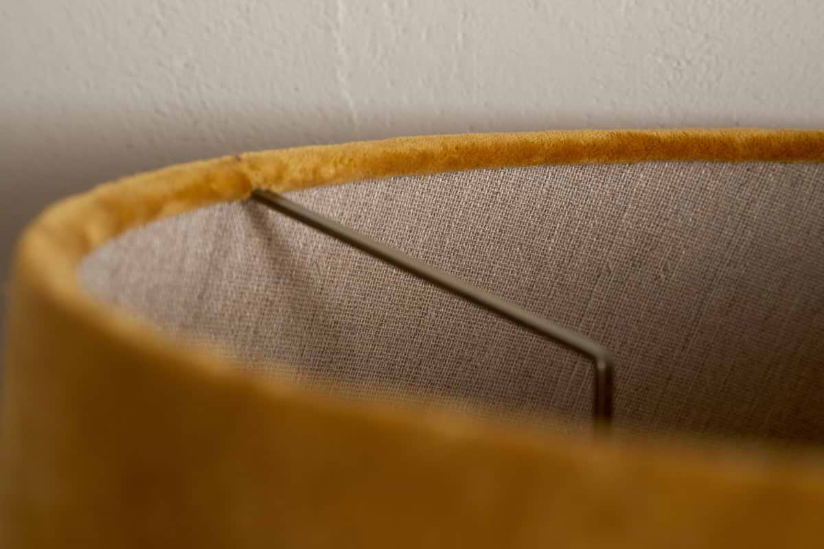 Close-up of the Batakha Velvet & Linen Lampshade in Dark Ochre by nkuku, highlighting its metal frame and textured inner lining against a white wall.