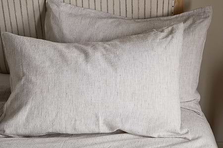 Two espresso-toned Borba Hemp & Cotton Housewife Pillowcases from nkuku rest against a matching headboard and bedsheet, creating a coordinated and minimalist bedroom look.
