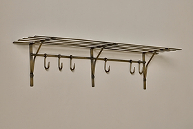 The nkuku Basti Iron Storage Shelf in antique brass features a vintage-style slatted top shelf and six hooks, mounted on a light wall for classic elegance and sturdy storage.
