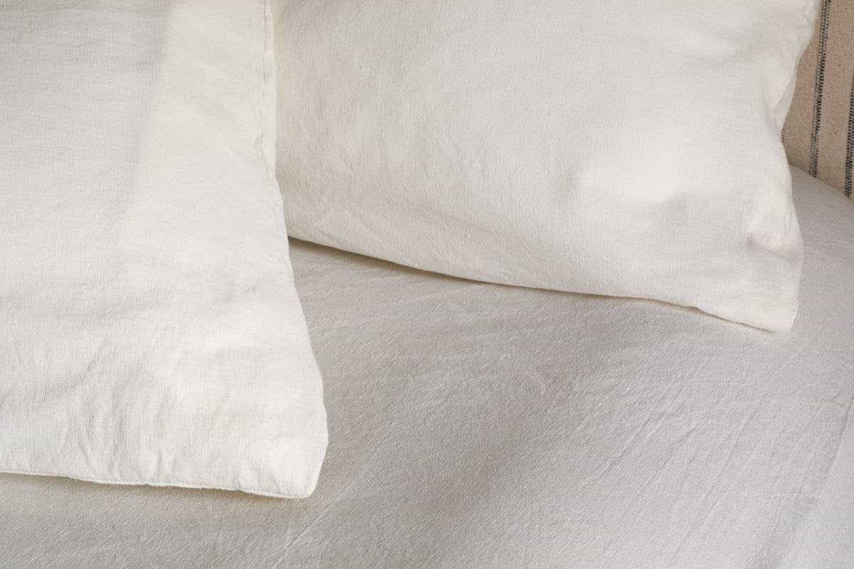 A close-up of two Cela Hemp & Cotton Housewife Pillowcases by nkuku in natural, featuring breathable fabric and a soft, clean look on a neatly made bed with white linens.