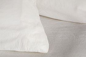 Close-up of two Cela Hemp & Cotton Housewife Pillowcases in Natural by nkuku, shown with a white bedsheet. Their breathable fabric creates a clean, cozy look, ideal for various bedroom styles.