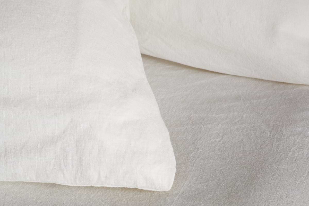 Close-up of two Cela Hemp & Cotton Housewife Pillowcases in Natural by nkuku, shown with a white bedsheet. Their breathable fabric creates a clean, cozy look, ideal for various bedroom styles.