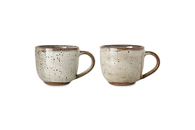 The nkuku Cam Coffee Mug - Mocha (Set of 2) features rustic mugs with handles, reactive speckled beige glaze, brownish rims, textured patterns, slightly rounded shapes, and warm brown unglazed bases displayed side by side on white.