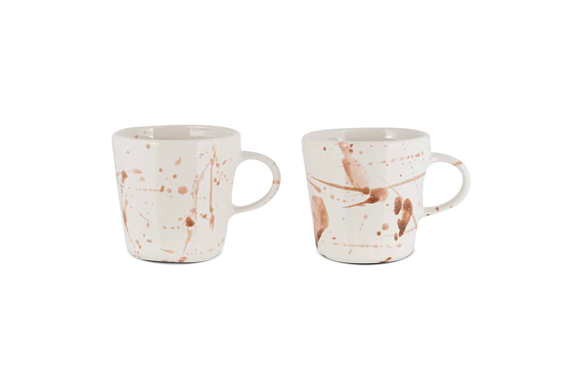 The nkuku Canela Mug - Dusty Terracotta (Set of 2) features two ceramic mugs with handles, each showcasing a unique brown splatter pattern for an artisanal look. The mugs are displayed against a plain white background.